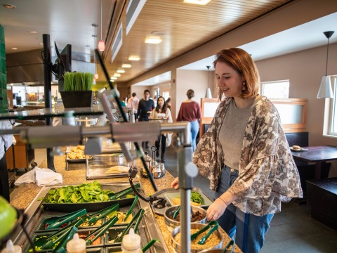Marnie Monogue stands at a counter with food choices in the dining hall