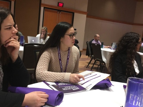 three students at table listening to a speaker at 2019 education summit