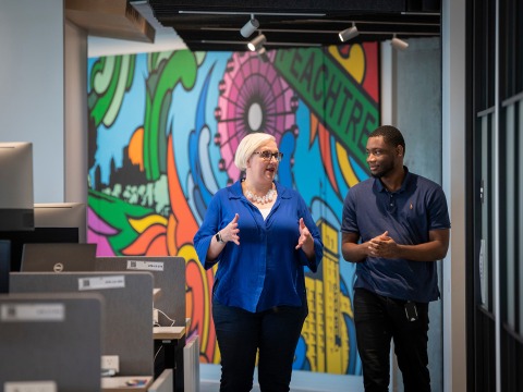 Carlton Segbefia and a co-worker talk as they walk past a colorful mural