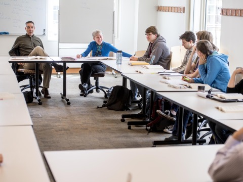 A professor and students gather for discussion around a table.