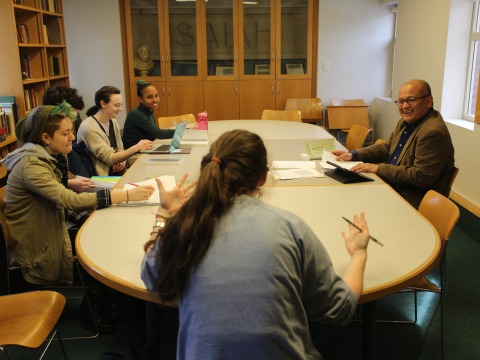 A professor talks with students gathered around a table.