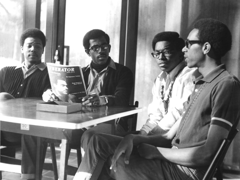 A group of four young men gather around a table.
