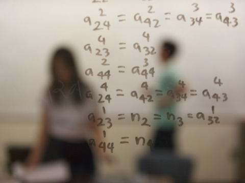 Math equations are written on a window, behind which are sillhouetes of people.