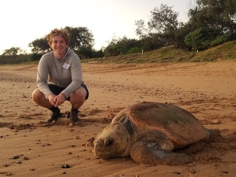 Crys kneels on the beach next to a large turtle.