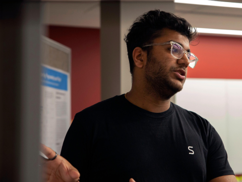 A young man gestures toward his poster while speaking to attendees.