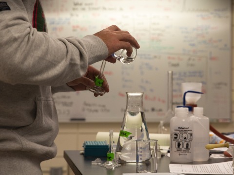 A student pours a solution from a flask into a test vial.