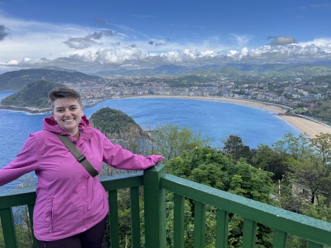 Sophie Noyes leans on a short railing that reveals a beautiful crystal blue lake.