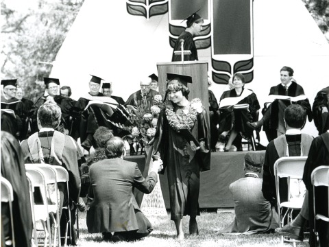 A student with a flower necklace around their neck walks down the center aisle at the 1989 Commencement ceremony. Courtesy of Grinnell College Special Collections & Archives. 