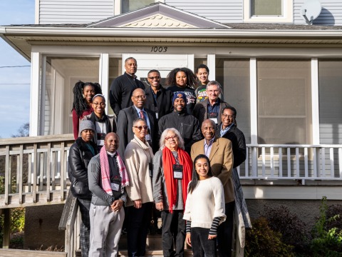A group of people stand on the steps of an old two-story house