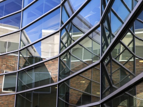 Wall-to-wall windows in the Noyce Science Center's courtyard reflect a blue sky.