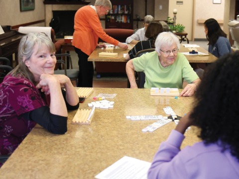 people play dominoes at 2 tables, one smiles at the camera