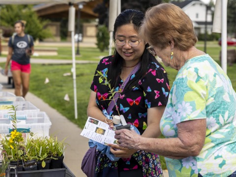 A farmer’s market vendor speaks to a student over a brochure.