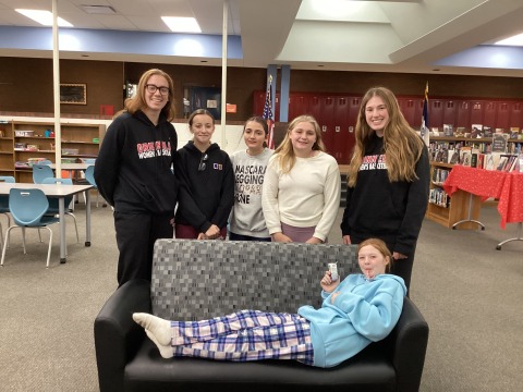 Two college students and middle schoolers pose behind a couch where a middle schooler lays. They all smile.