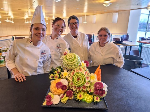 People in white chef outfits in front of carved fruit