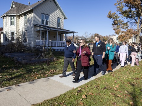 Susan Sanning leading a group of adults walking down the sidewalk past a white house.