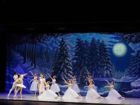dark snow scene on stage with a man and a woman in white dancing ballet