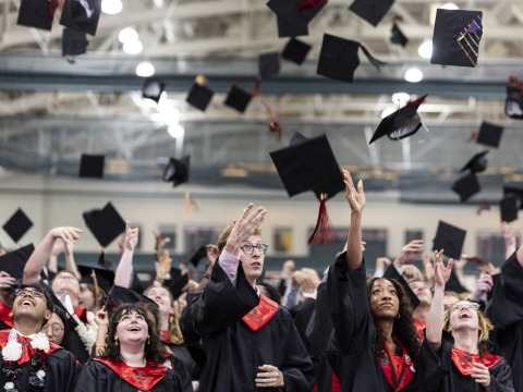 Students wearing black and red graduation regalia throw their caps in the air