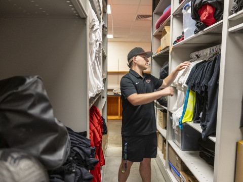 Luke Thompson putting away jerseys in the athletic closet.