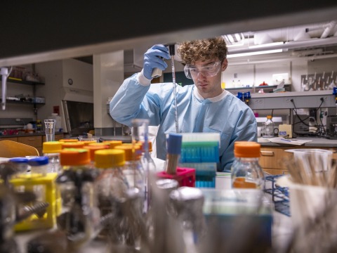 A young man in laboratory garb works with soil samples in a lab.