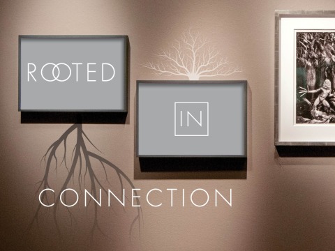 Two framed gray panels on a wall display the words "ROOTED" and "IN" with tree roots and branches extending from the frames, accompanied by the word "CONNECTION" below.
