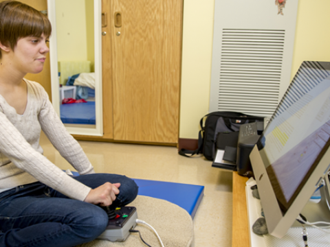 Jennifer Brooks ’15 sits on a blue gymnastics mat, facing a Mac on a table about 4 inches off the floor.