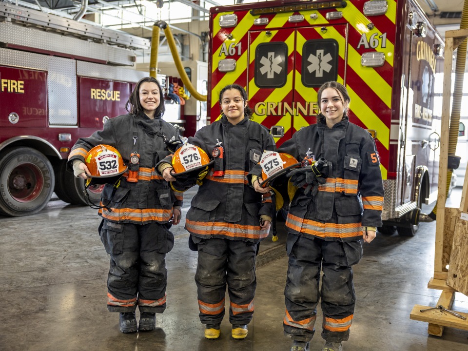 Three students with fire equipment on and ambulance behind them. 