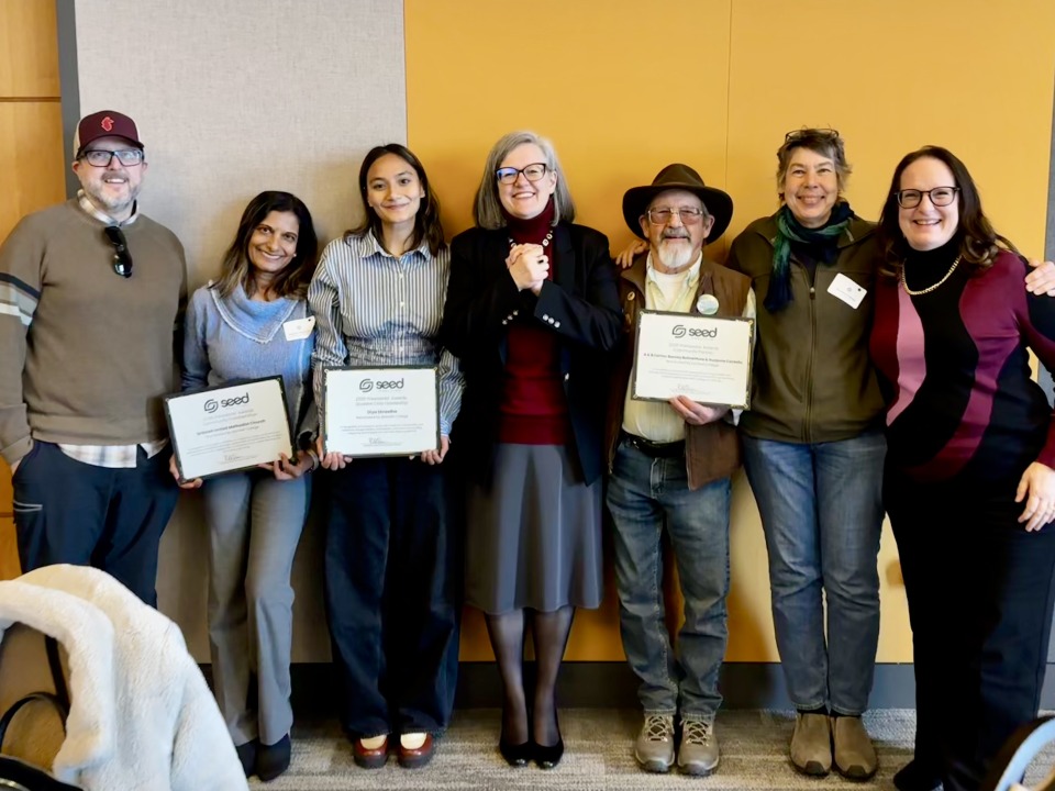 Seven people standing in a line, three holding certificates