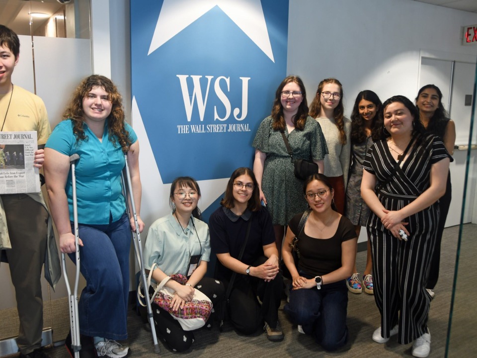 Ten students posing around a blue and white sign that reads "WSJ Wall Street Journal"