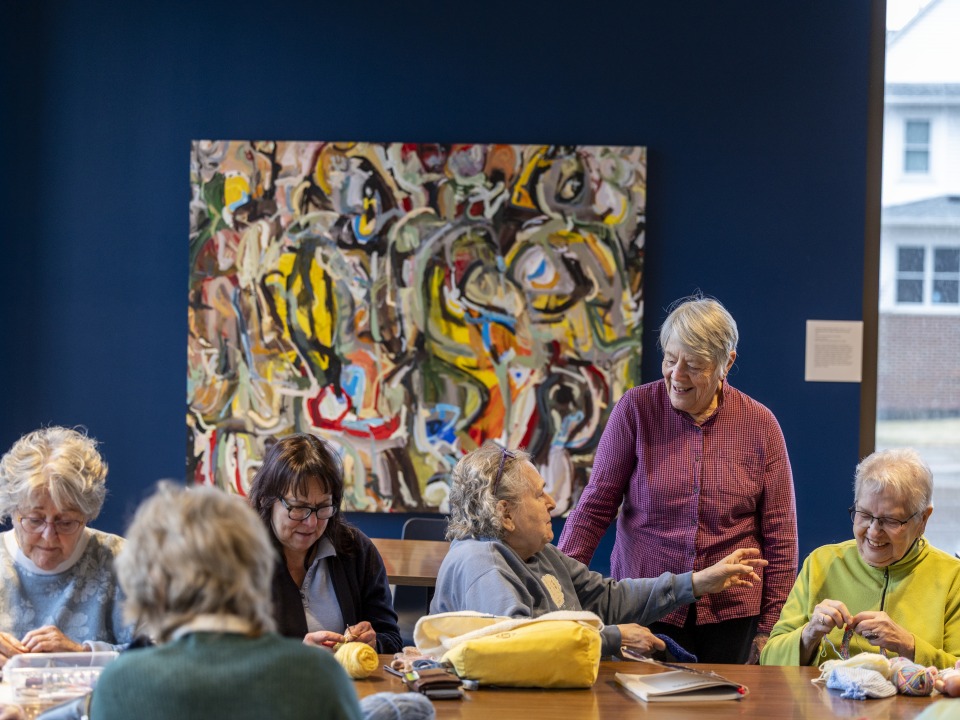 Six older women sitting around a table and knitting