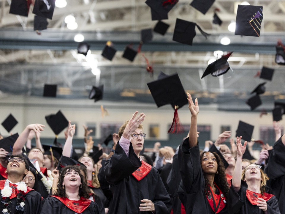 Students wearing black and red graduation regalia throw their caps in the air