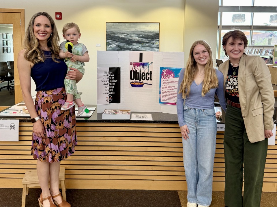 A woman holding a young child stands on the left of a poster board reading "I Object" and two students stand together on the right