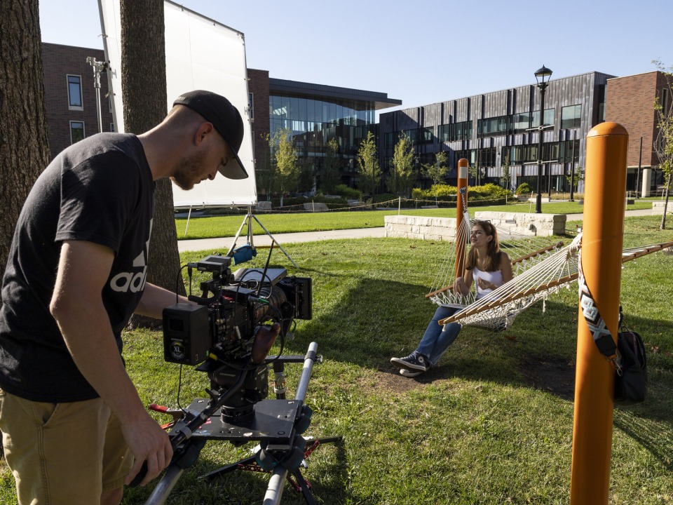 man with a video camera on campus with girl in hammock
