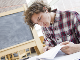 A man in a plaid shirt reads a book. A blackboard is visible in the background