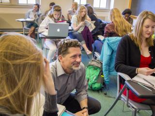 Tyler Roberts squatting next to students while teaching a course