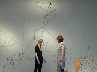 Two students stand in front of a large sculpture made of many segments of straight wire.