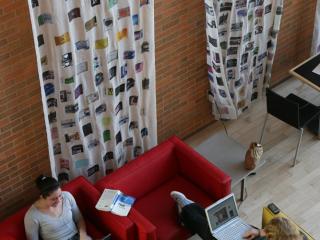 Two Grinnellians use theit laptops in the Grill on bright yellow and red chairs
