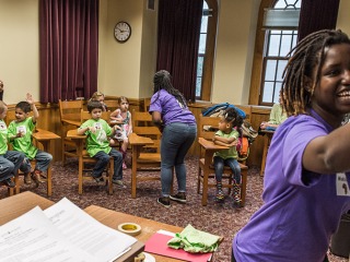 two college students in purple tshirts interact with younger children wearing green ones