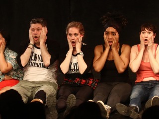 Neofuturists sitting on the floor in a row with surprised expressions