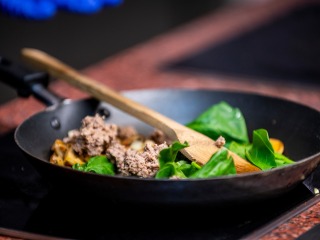 A small saute pan with fresh spinach leaves and ground meat, ready to be tossed together