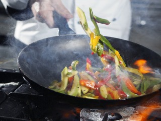 Vegetables being tossed in a skillet over a flame on a stove