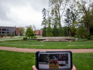 Smart phone in foreground showing virtual commencement in front of empty outdoor commencement stage in background