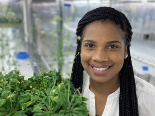 Shanice Webster smiles while standing next to plants in her research laboratory.