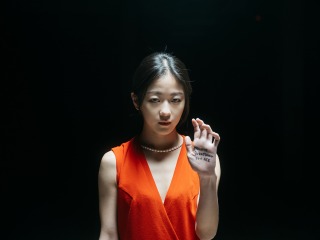 A young woman in an orange dress holds up her hand, which has writing on the palm