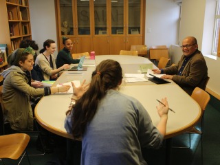 A professor talks with students gathered around a table.