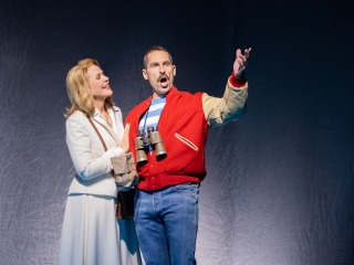 Renée Fleming in blazer and skirt and Kyle Ketelsen wearing a red letter jacket with binoculars and singing