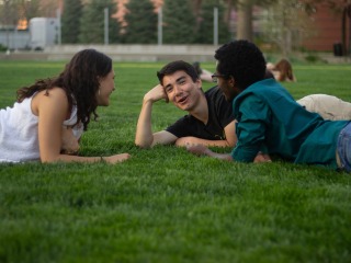3 students talking lay in a circle on the green lawn