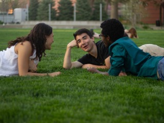 3 students talking lay in a circle on the green lawn