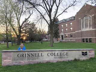 MJ Uzzi poses with the Grinnell College sign at sunrise