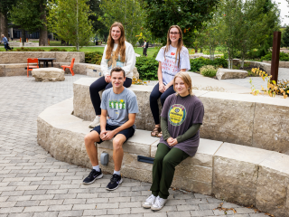 Four students sit on a gray brick ledge.