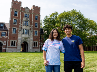 Kylie Ann Smith '27 and Preston Yoshida '27 stand in a green Mac Field in front of a looming Gates Tower.